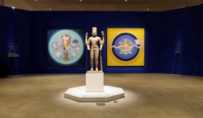 A Cambodian statue of Vishnu from the early 800s stands between paintings by Desmond Lazaro in Avatar: Forms of Vishnu at the Art Gallery of New South Wales in Sydney, on view until October 5, 2026. PHOTO: Jenni Carter, Art Gallery of New South Wales